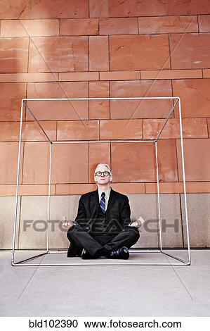 Stock Image - Caucasian businessman practicing yoga on sidewalk. Fotosearch