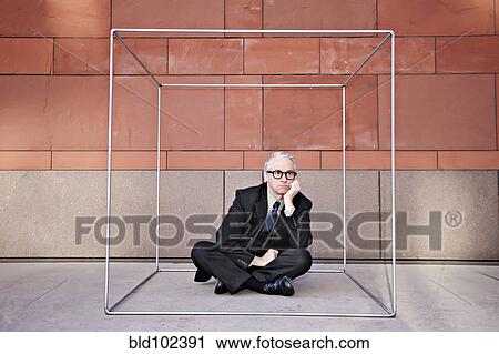 Stock Image - Caucasian businessman sitting inside of box. Fotosearch