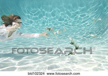 Picture - Caucasian businesswoman reaching for money underwater. Fotosearch