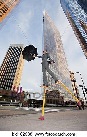 Stock Photo - Caucasian businesswoman walking on stilts in urban environment. Fotosearch