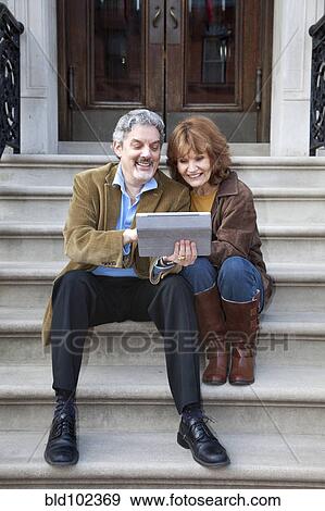 Stock Photo - Caucasian couple using digital tablet on front stoop. Fotosearch