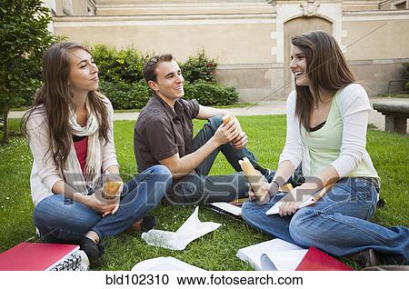 Stock Image - Caucasian friends eating lunch on grass. Fotosearch