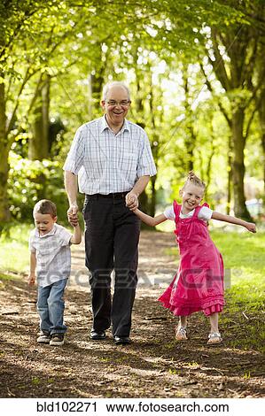 Stock Image - Caucasian grandfather and grandchildren walking in woods. Fotosearch