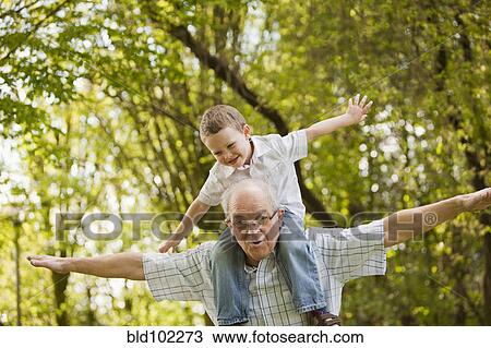Stock Image - Caucasian grandfather carrying grandson on shoulders. Fotosearch