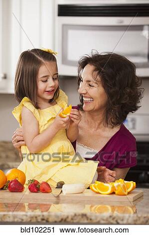Stock Image - Caucasian grandmother and granddaughter eating fruit. Fotosearch