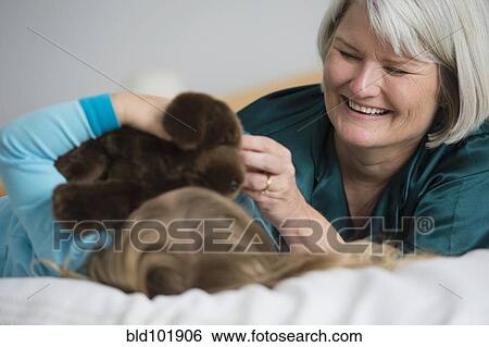 Stock Photograph - Caucasian grandmother laying on bed with granddaughter. Fotosearch