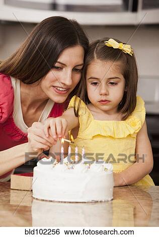 Stock Photograph - Caucasian mother and daughter lighting birthday candles. Fotosearch