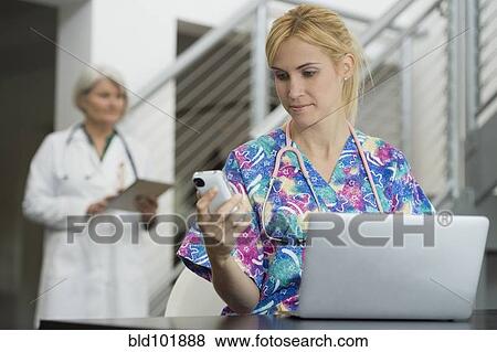 Stock Photo - Caucasian nurse using cell phone and laptop. Fotosearch
