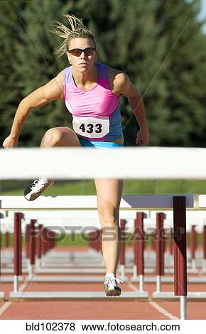 Stock Photo - Caucasian runner jumping over hurdles. Fotosearch