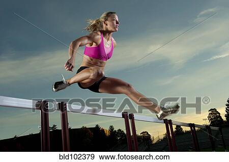 Stock Photo - Caucasian runner jumping over hurdles. Fotosearch