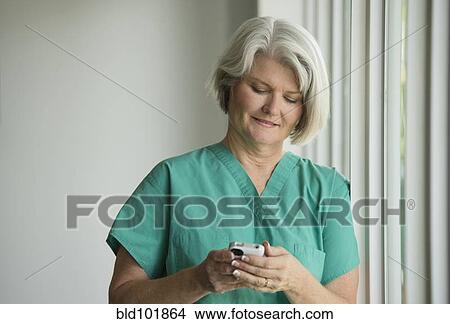 Picture - Caucasian surgeon in scrubs using cell phone. Fotosearch