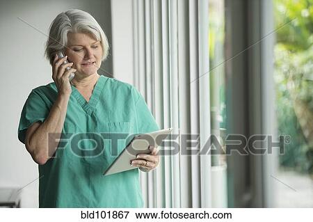 Caucasian surgeon in scrubs using cell phone and digital tablet View Large Photo Image Stock Photo - Caucasian surgeon in scrubs using cell phone and digital tablet. Fotosearch