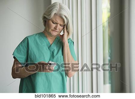 Stock Photography - Caucasian surgeon in scrubs using cell phone. Fotosearch