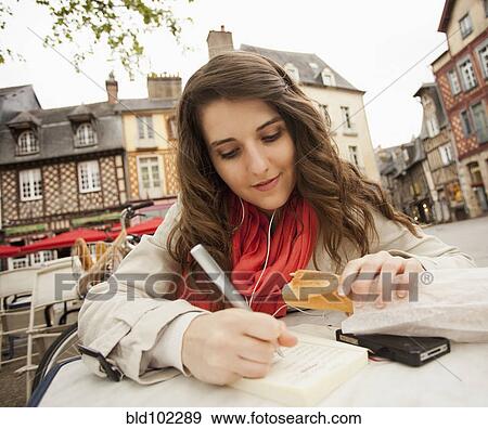 Stock Photo - Caucasian woman eating bread and writing in book. Fotosearch