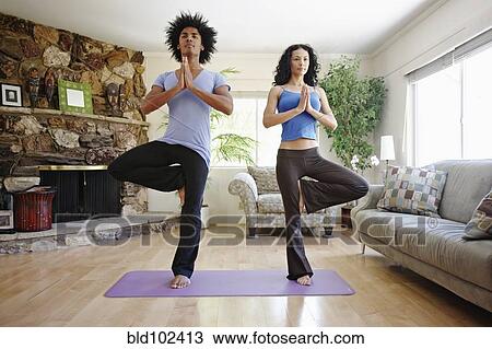 Stock Image - Couple practicing yoga in living room. Fotosearch