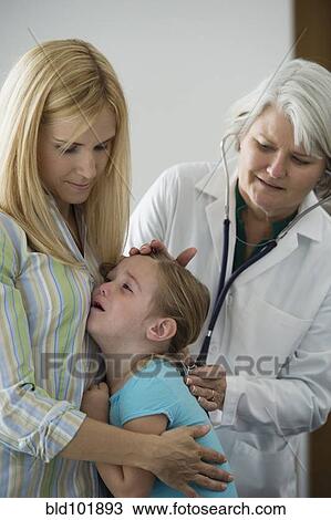 Stock Image - Crying girl having checkup in doctor's office. Fotosearch