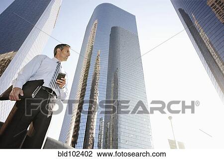 Stock Image - Hispanic businessman holding cell phone and notebook outdoors. Fotosearch