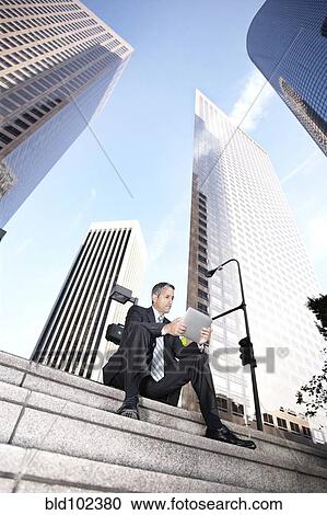 Stock Image - Hispanic businessman sitting on steps with digital tablet. Fotosearch
