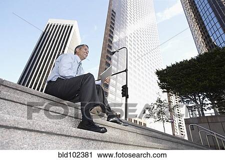 Stock Image - Hispanic businessman sitting on steps with digital tablet. Fotosearch