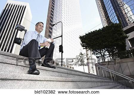 Stock Image - Hispanic businessman sitting on steps drinking coffee. Fotosearch