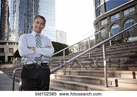 Stock Photography - Hispanic businessman standing outdoors with arms crossed. Fotosearch