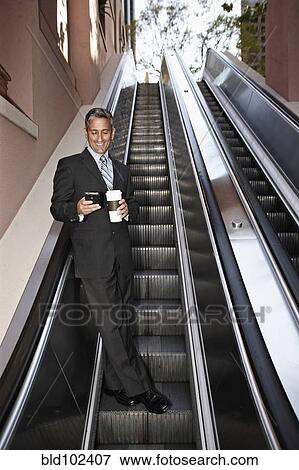 Hispanic businessman text messaging on escalator View Large Photo Image Stock Photo - Hispanic businessman text messaging on escalator. Fotosearch