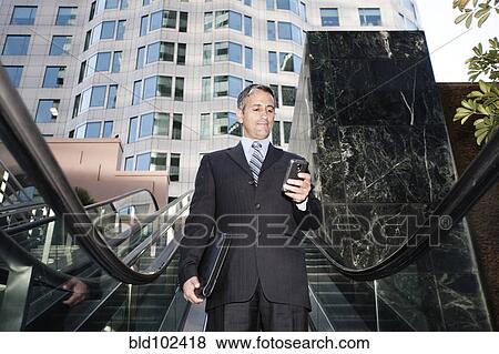 Hispanic businessman text messaging on escalator View Large Photo Image Stock Photo - Hispanic businessman text messaging on escalator. Fotosearch