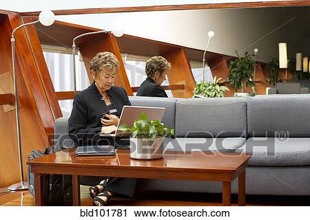 Stock Image - Hispanic businesswoman using laptop on sofa. Fotosearch