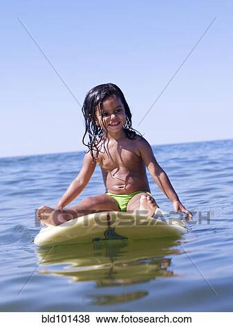 Stock Photo - Hispanic girl sitting on surfboard. Fotosearch
