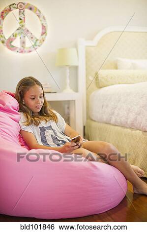 Stock Photograph - Hispanic girl text messaging on cell phone in bedroom. Fotosearch