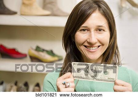 Stock Image - Hispanic woman holding cash in shoe store. Fotosearch