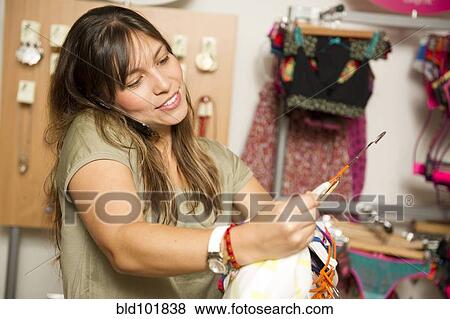 Stock Photo - Hispanic woman holding clothing and talking on cell phone in store. Fotosearch