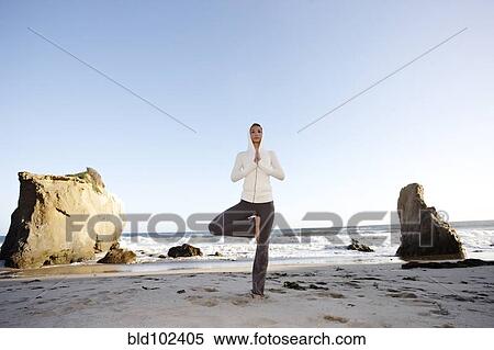 Stock Photography - Hispanic woman practicing yoga on beach. Fotosearch