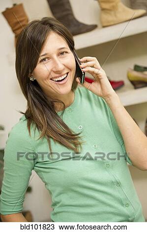 Stock Image - Hispanic woman talking on cell phone in shoe store. Fotosearch