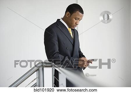 Stock Image - Mixed race businessman text messaging on cell phone. Fotosearch