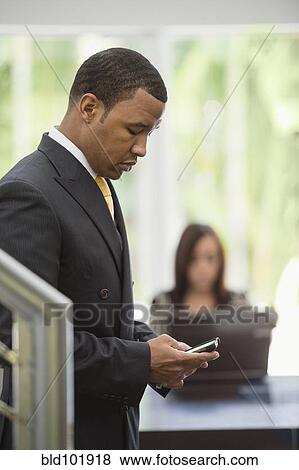 Stock Photo - Mixed race businessman text messaging on cell phone. Fotosearch