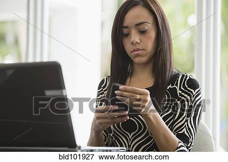 Stock Photo - Mixed race businesswoman text messaging on cell phone. Fotosearch