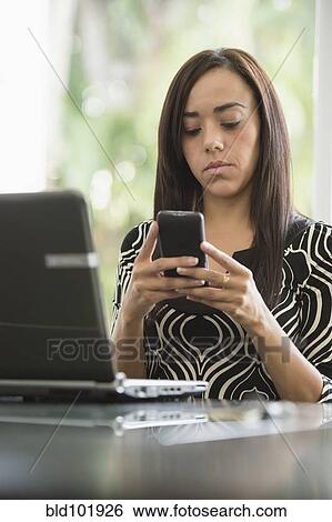 Stock Photograph - Mixed race businesswoman text messaging on cell phone. Fotosearch
