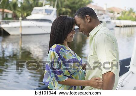 Picture - Mixed race couple hugging near waterfront. Fotosearch