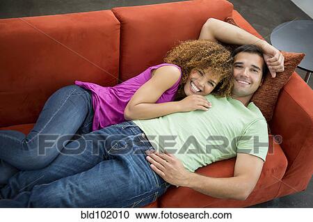 Stock Image - Mixed race couple laying on sofa together. Fotosearch