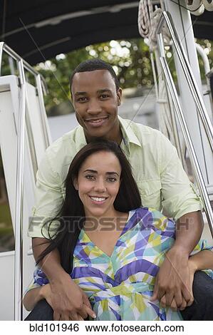 Stock Photograph - Mixed race couple sitting together on boat. Fotosearch