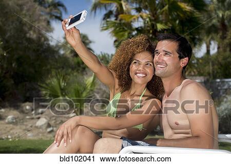 Stock Image - Mixed race couple taking self-portrait with cell phone. Fotosearch