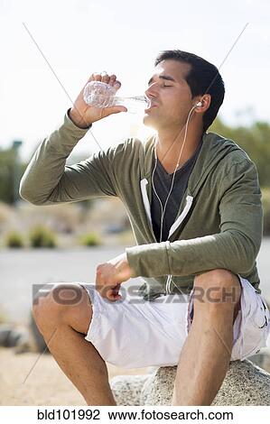 Stock Image - Mixed race man drinking water after exercise. Fotosearch