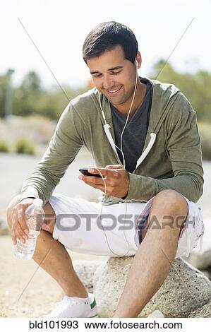 Stock Image - Mixed race man drinking water after exercise and listening to music. Fotosearch