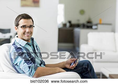 Mixed race man sitting on sofa holding cell phone View Large Photo Image Stock Photograph - Mixed race man sitting on sofa holding cell phone. Fotosearch