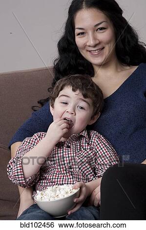 Stock Photograph - Mixed race mother and son eating popcorn. Fotosearch