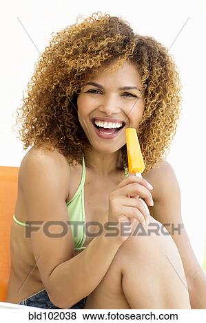 Stock Photo - Mixed race woman eating popsicle. Fotosearch