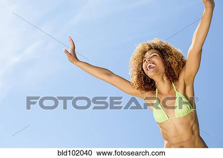 Stock Image - Mixed race woman in bikini with arms raised. Fotosearch