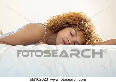 Stock Image - Mixed race woman laying on bed. Fotosearch