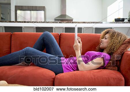 Mixed race woman laying on sofa using digital tablet View Large Photo Image Stock Photo - Mixed race woman laying on sofa using digital tablet. Fotosearch